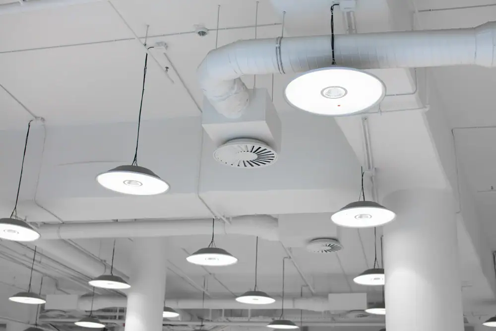 A white ceiling with exposed pipes, ducts, and several round, modern pendant lights—installed by expert electrician Cook and Will County, IL—hang at different heights, creating a clean, industrial look.
