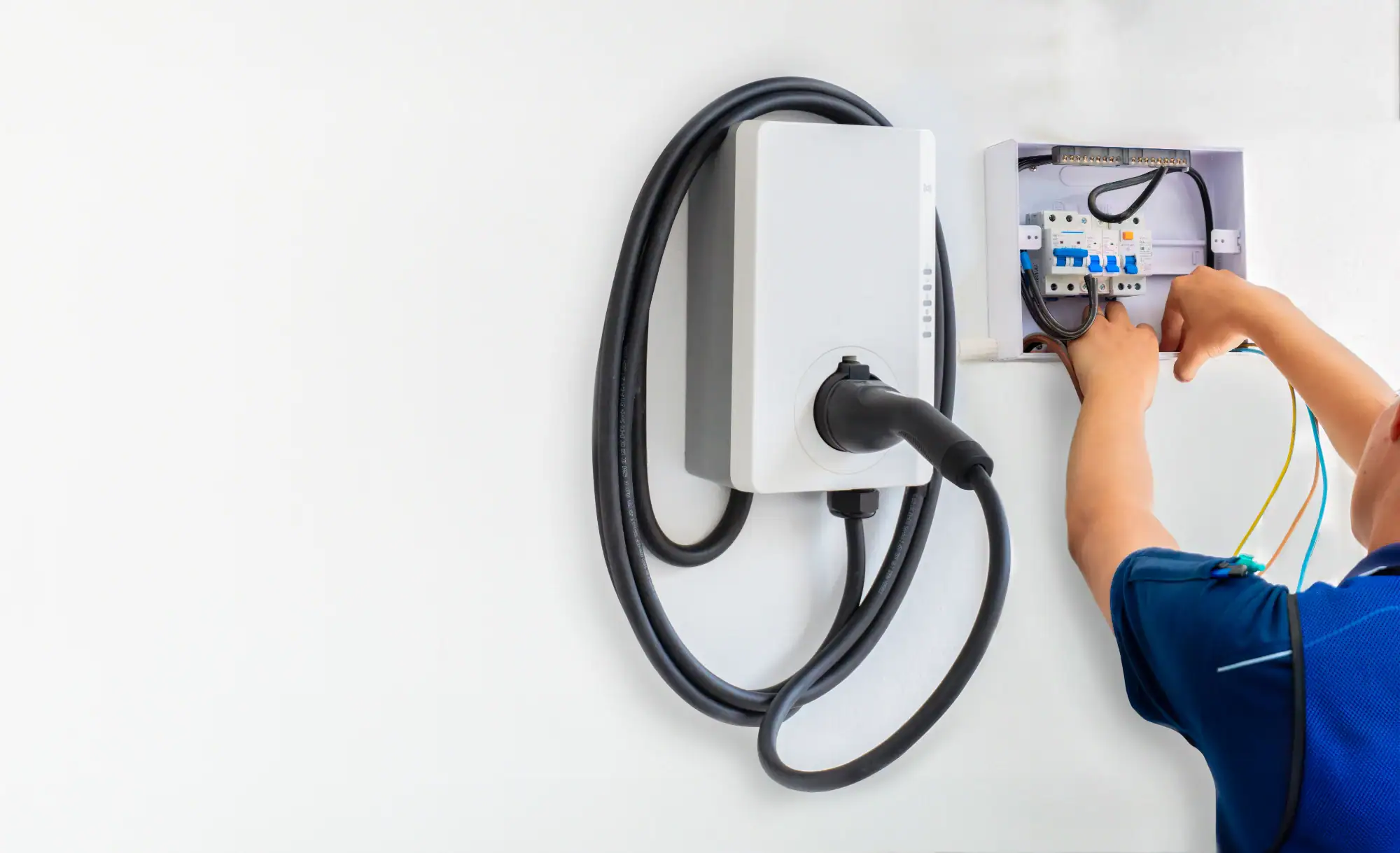 A person in a blue shirt installs or services an electric vehicle (EV) charging station on a white wall, with an electrical panel open and wires visible—professional Electrical Services Cook and Will County, IL.