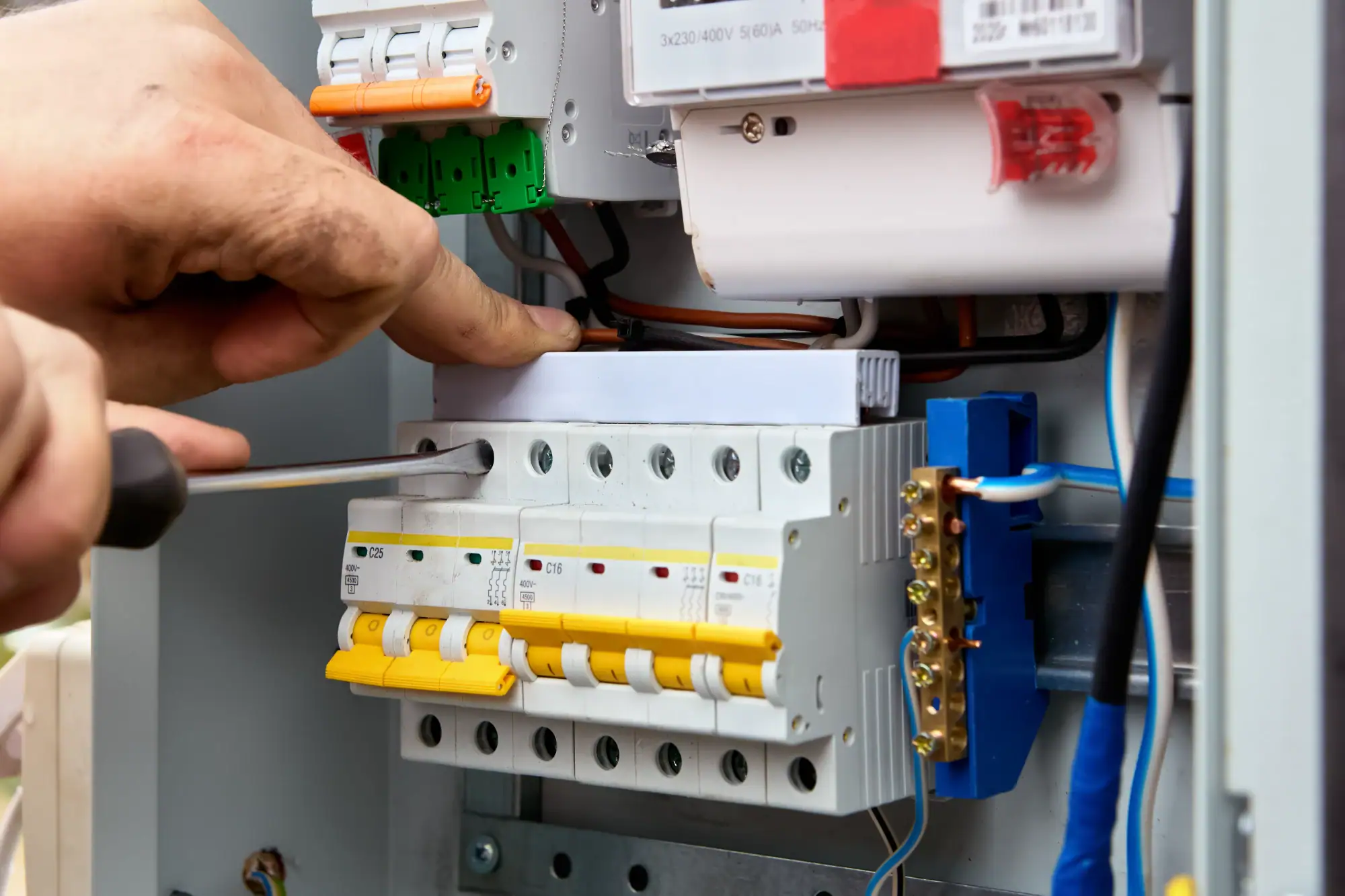 An electrician in Cook and Will County uses a screwdriver to adjust or install electrical circuit breakers inside a control panel, with various colored wires and components visible, showcasing expert IL Electrical Services.