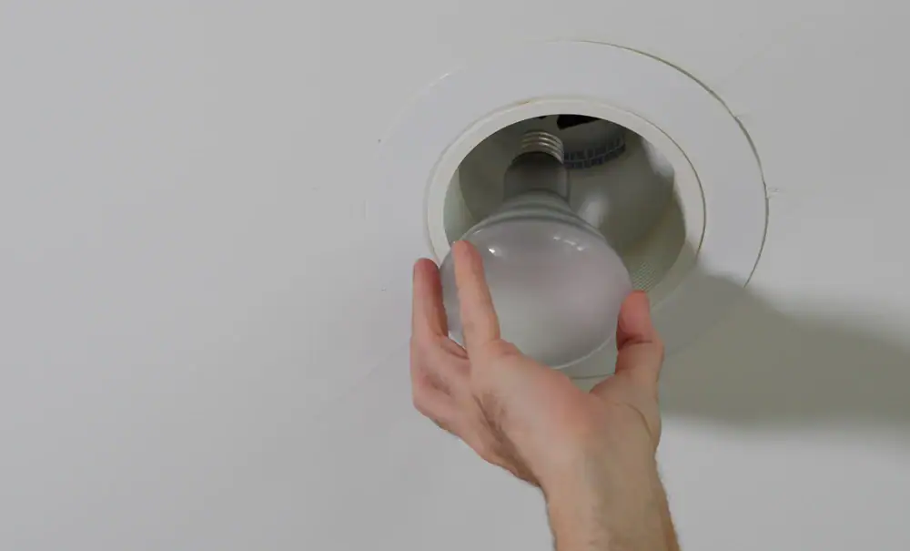 A person’s hand is installing or removing a light bulb from a recessed ceiling light fixture, demonstrating the care and expertise of an electrician Cook and Will County residents trust.