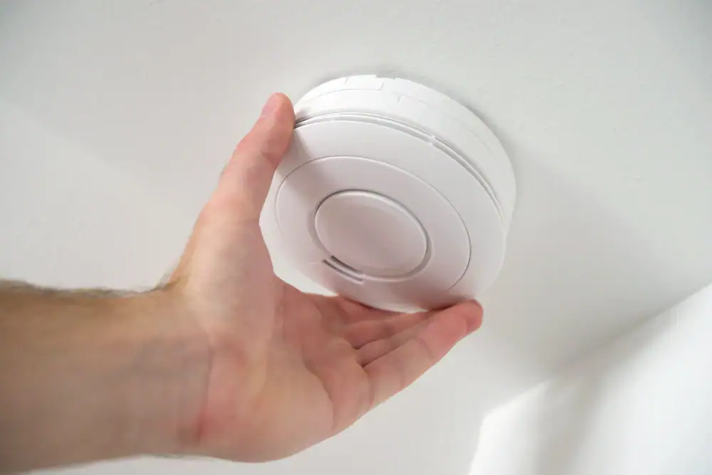 A close-up of a hand installing or adjusting a round, white smoke detector on a white ceiling—professional Electrical Services Cook and Will County, IL ensure safety for your home or business.