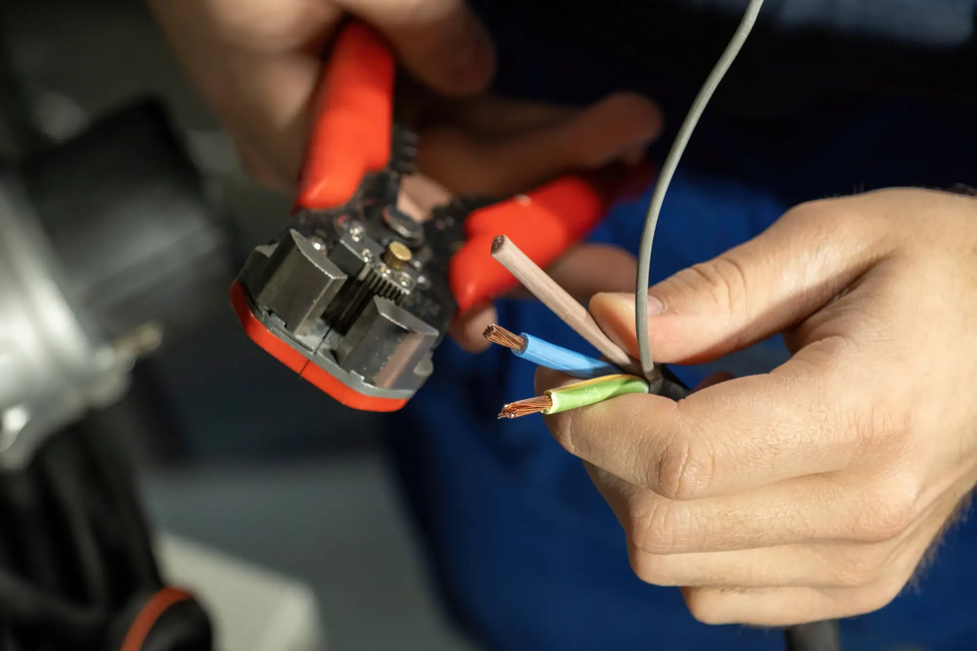 An electrician in Cook and Will County uses wire strippers with red handles to remove insulation from electrical wires, exposing copper cores in a bundle of black, blue, and green wires.