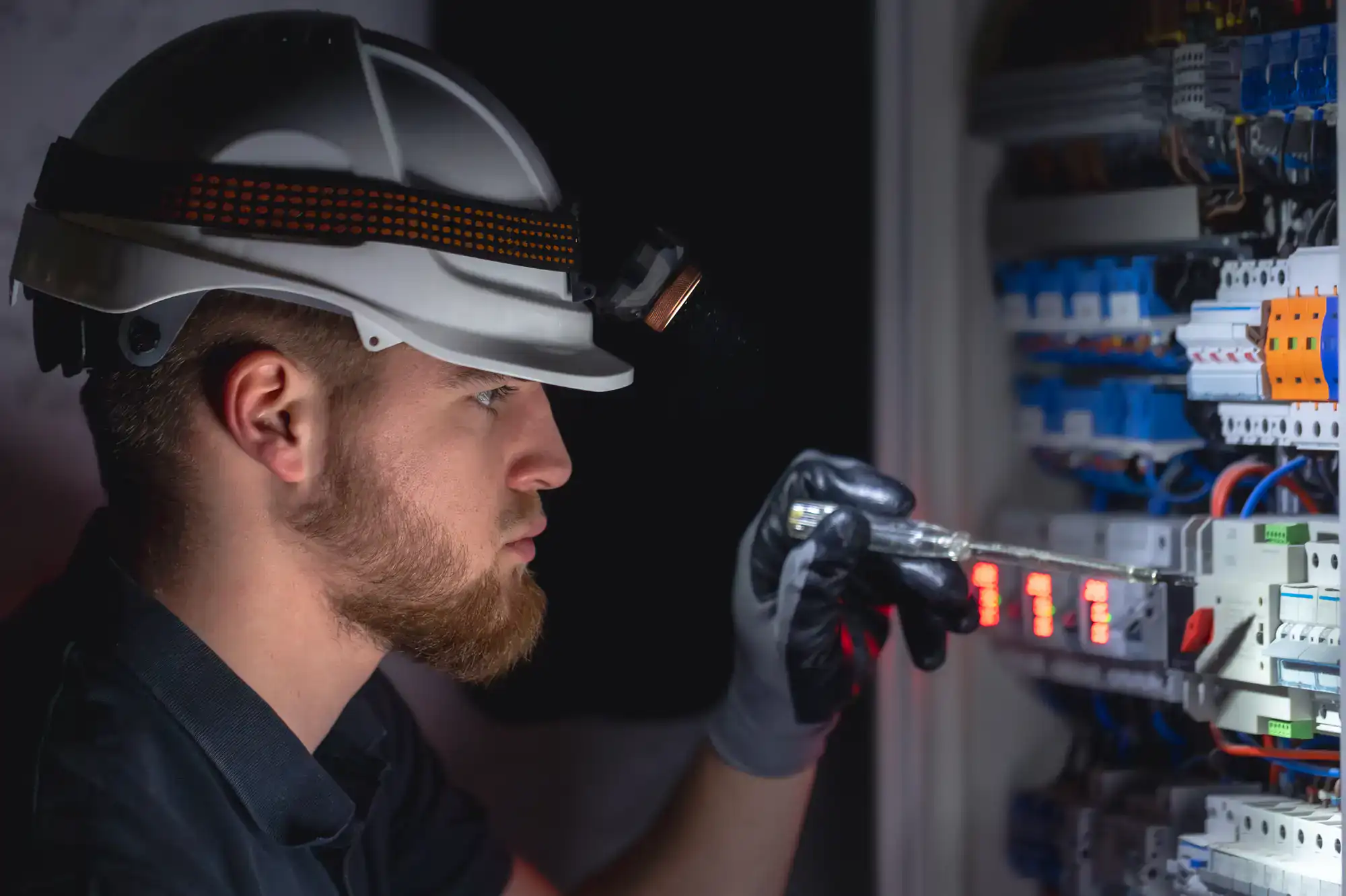 A skilled electrician with a yellow hard hat inspects a control panel at a job site in Chicago, IL. The worker is adjusting circuits and maintaining electrical equipment