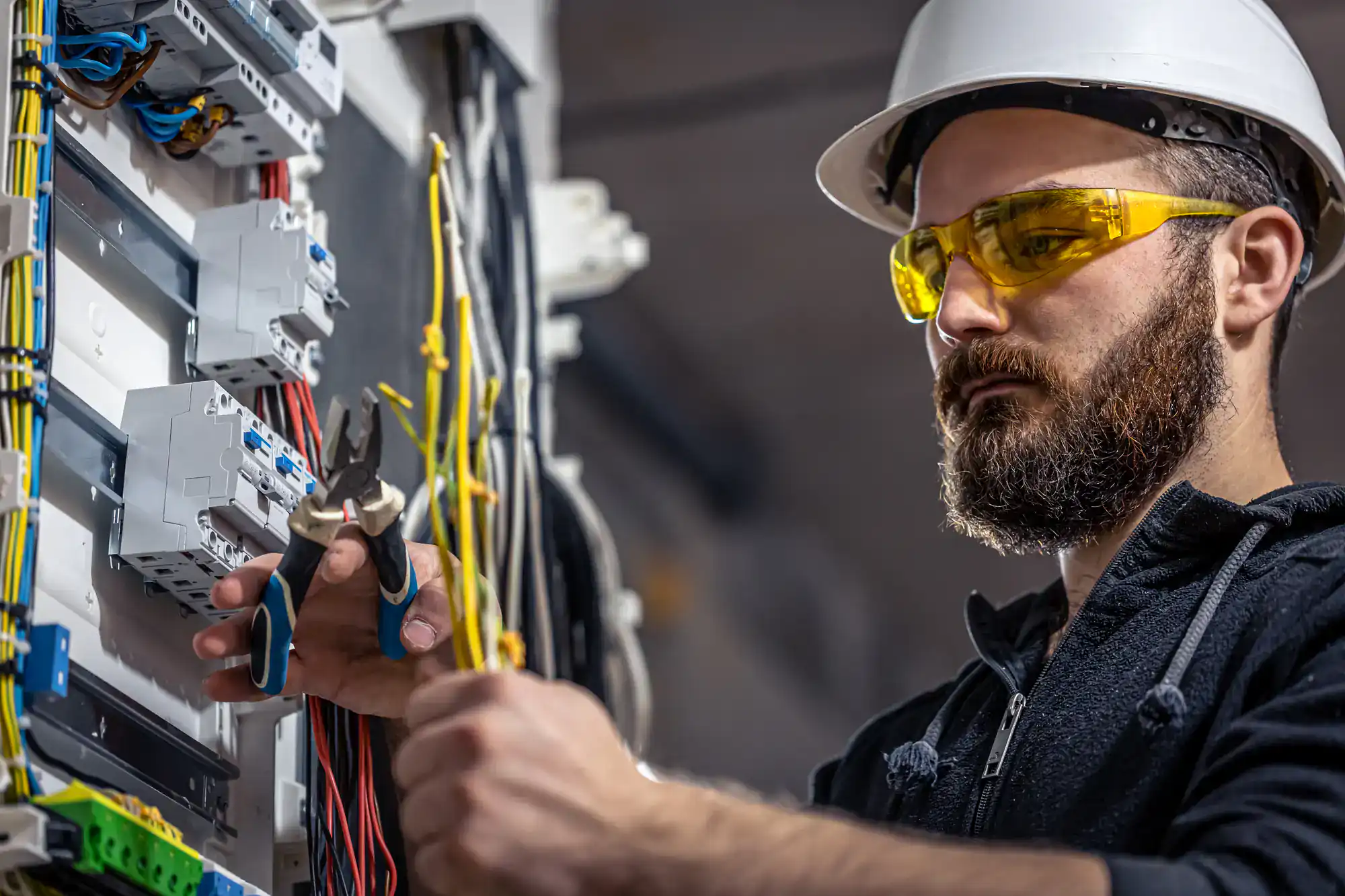 Electrician wearing a yellow hard hat installs electrical wiring in a residential property in Chicago, IL, Illinois. The worker is focused on ensuring safe and accurate wiring for the home’s electrical system